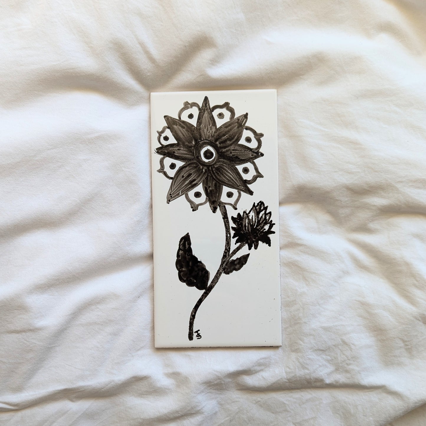 A ceramic tile with a ink illustration of a strange eyeball like flower. 